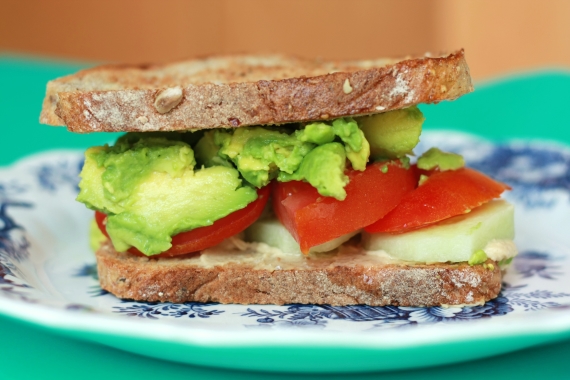 twee geroosterde boterhammen met daartussen hummus, tomaat, avocado en komkommer