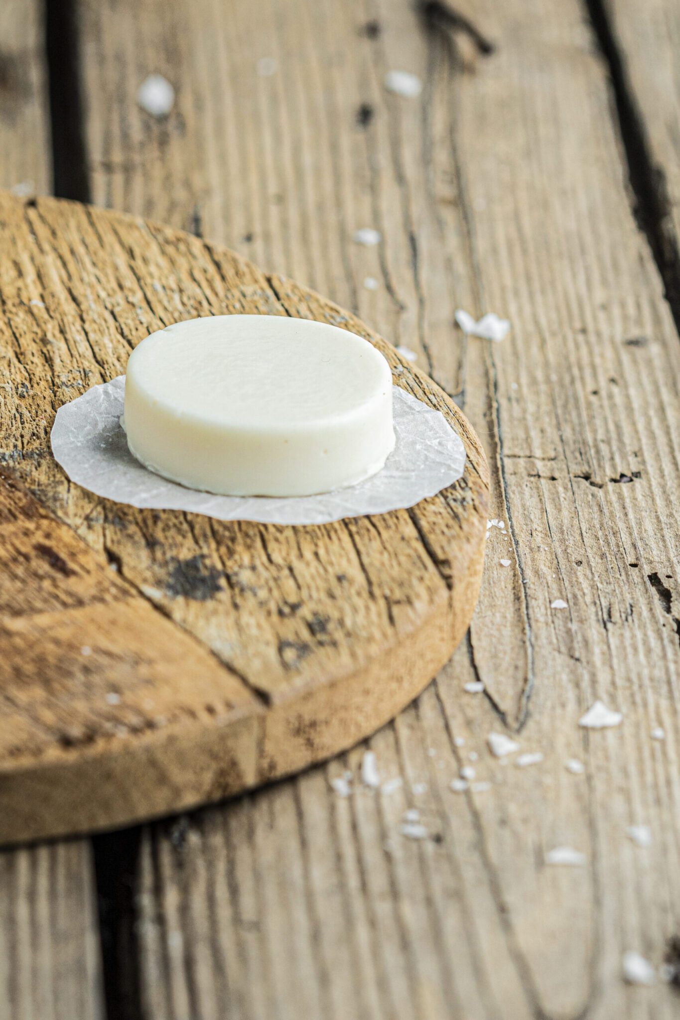 Foto van een rond blokje vegan kaas op een houten tafel.