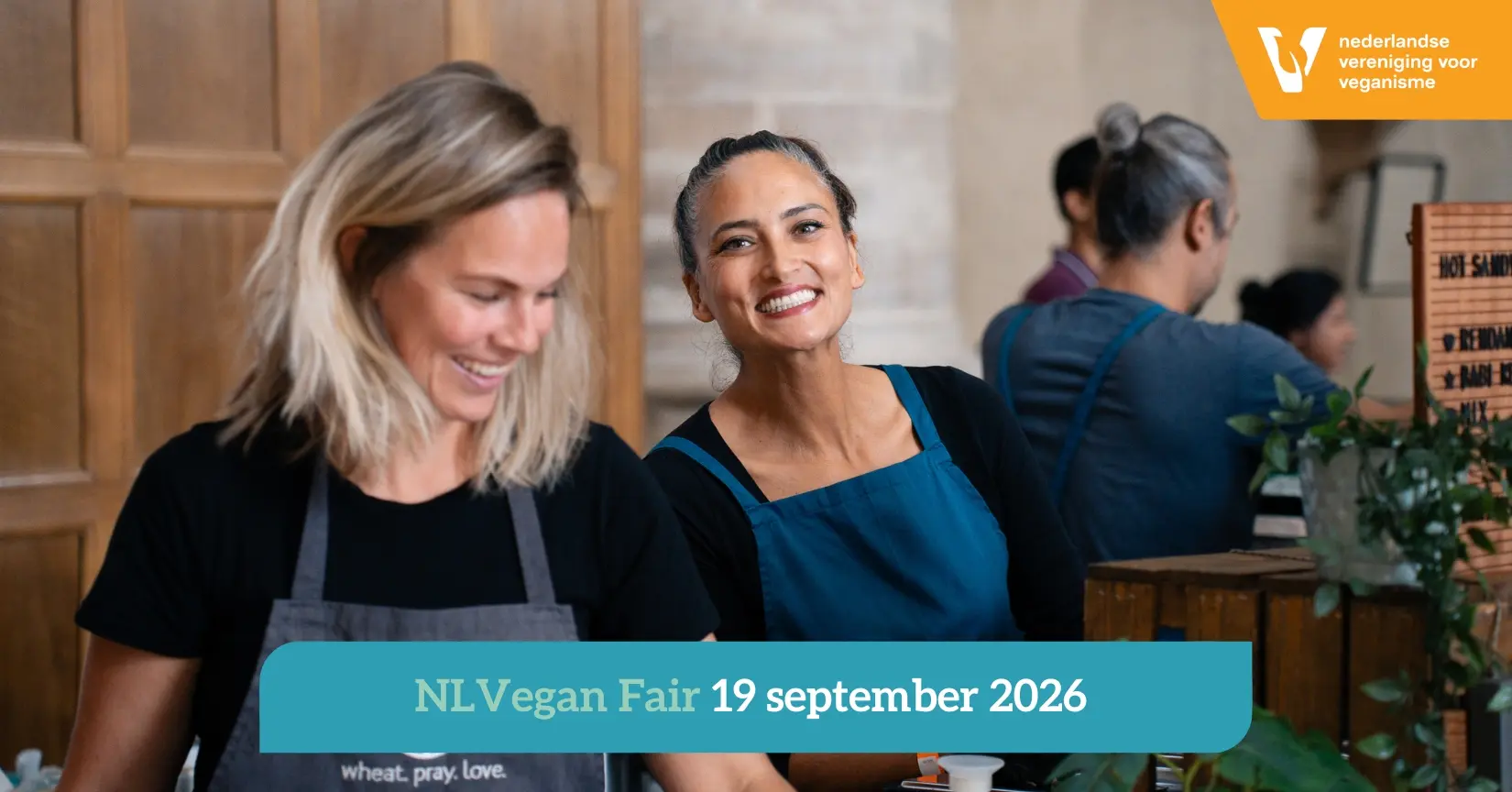 Afbeelding voor de NLVegan Fair 2026 met twee lachende standhouders die zich klaarmaken voor het evenement