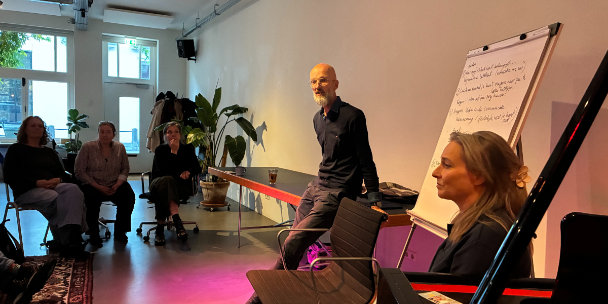 Trainer Rombout staat voor een groep, naast een flipover. Ook in beeld is Barbara Tiggeler.