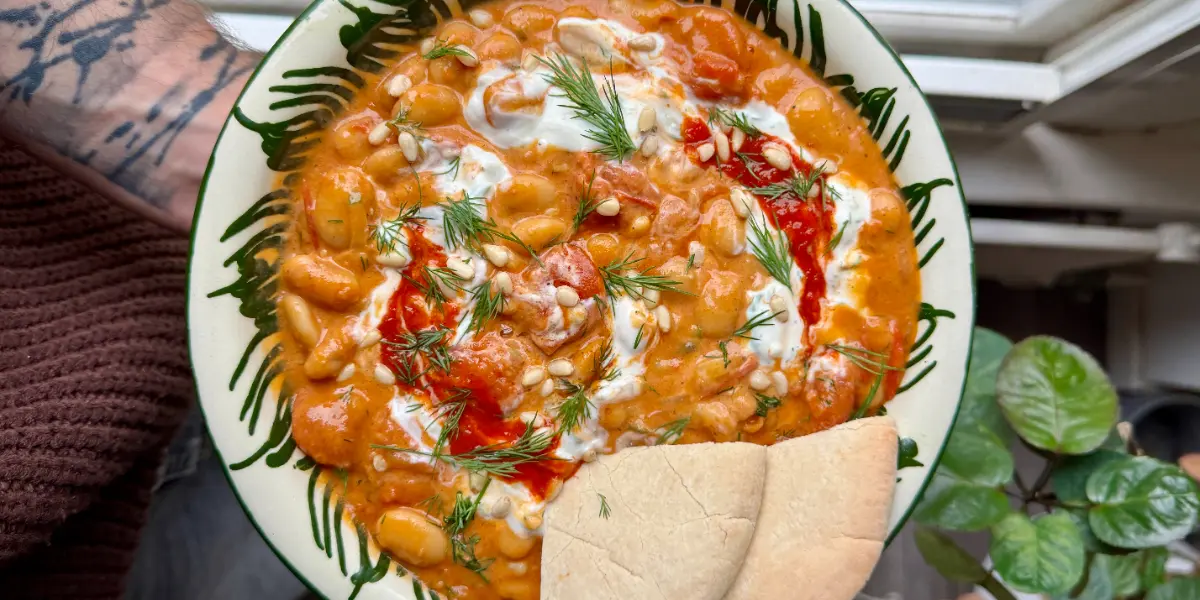 Een hand houdt een bord met een romige oranje curry vast.