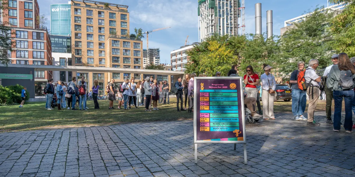 Programma-NLVegan-Fair-2025-Roactive Foto van een stoepbord met het programma van de NLVegan Fair, op straat voor een rij met mensen in Rotterdam.