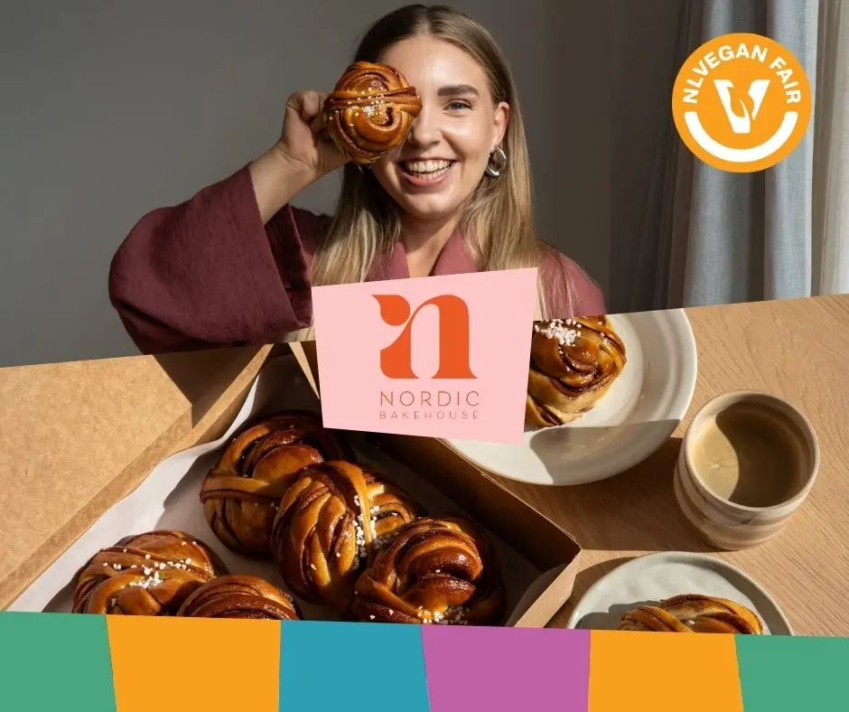 Een blije dame met baksels van Nordic Bakehouse met daarvoor het logo en het logo van NLVegan Fair