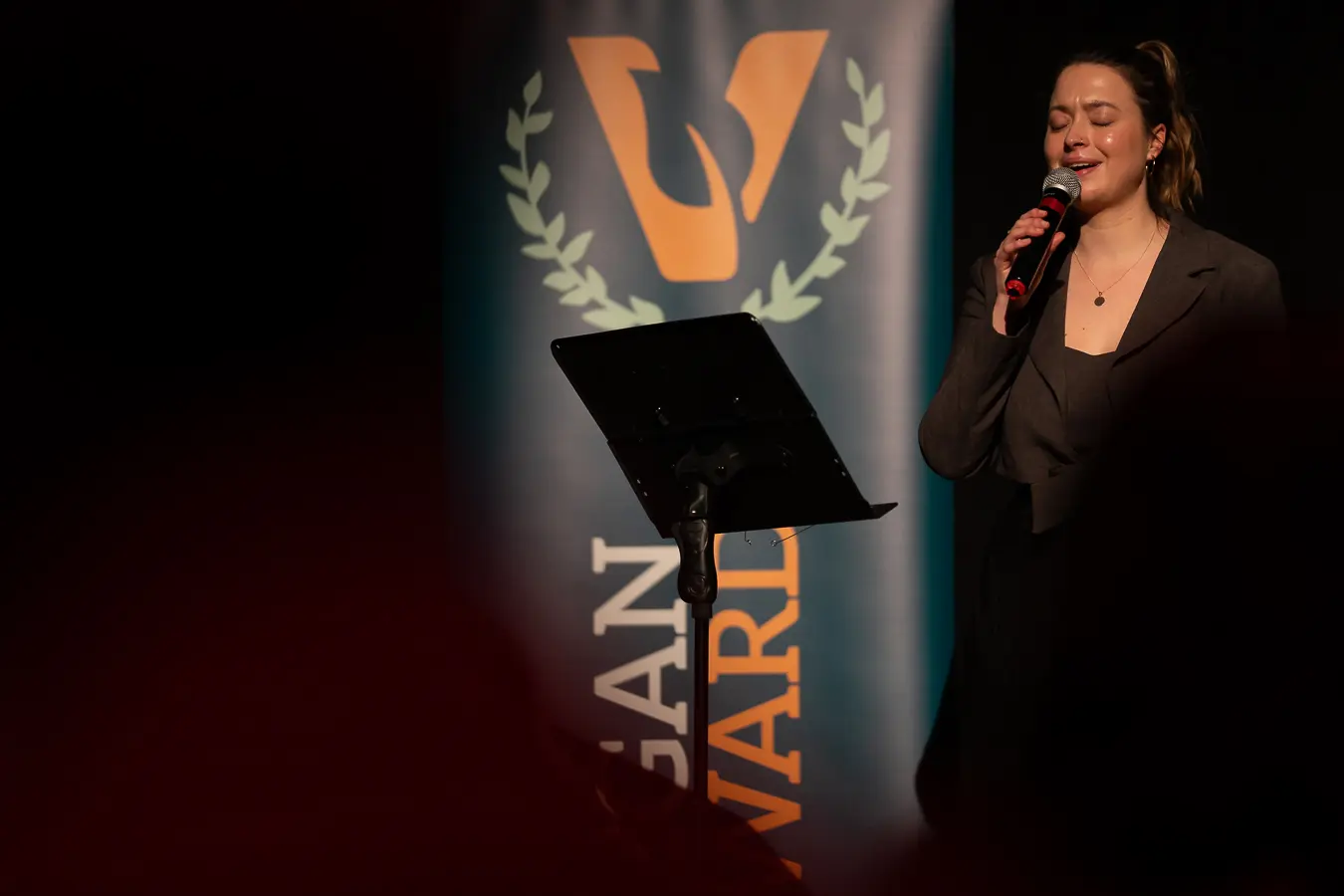 Vrouw die zingt met haar ogen dicht voor de Vegan Awards banner.