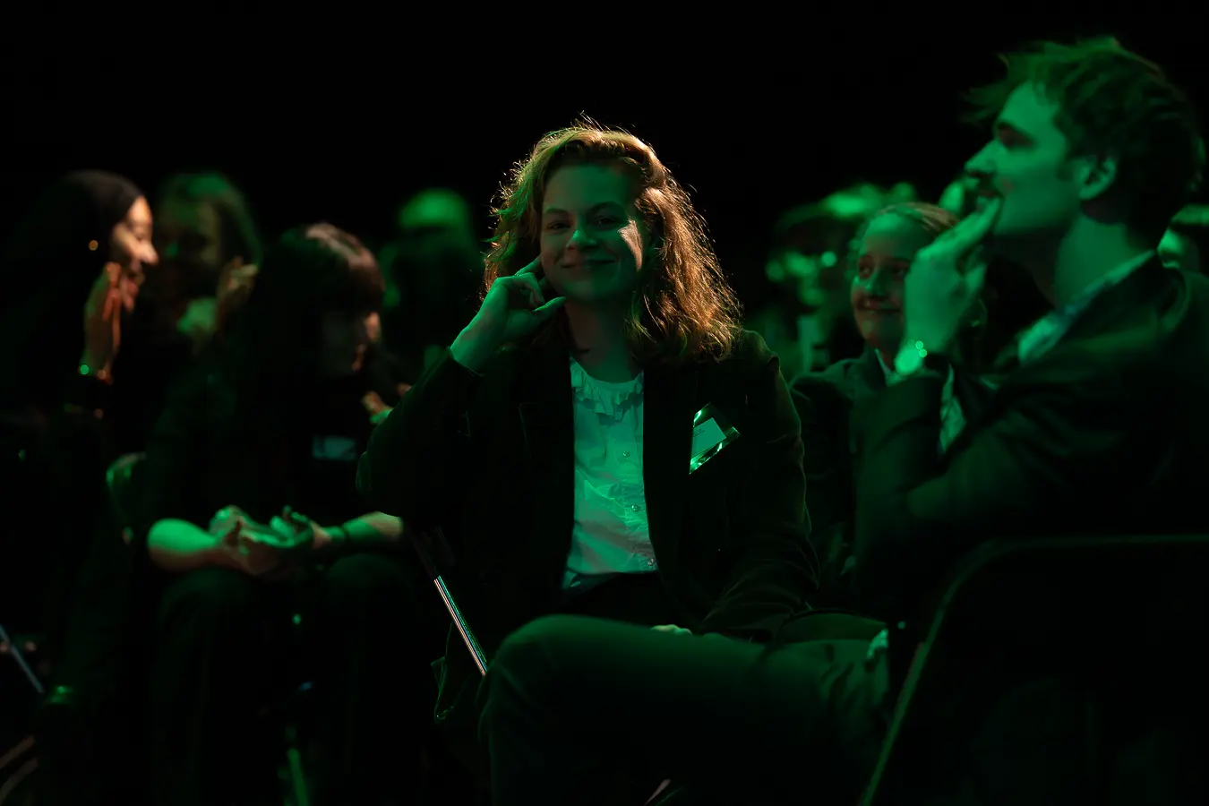 Dame in het publiek die lachend zit en de camera inkijkt.