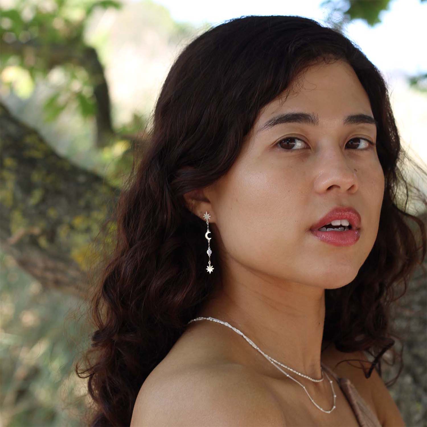 Vrouw met Garland universe lange zilveren oorbellen. Bomen op de achtergrond