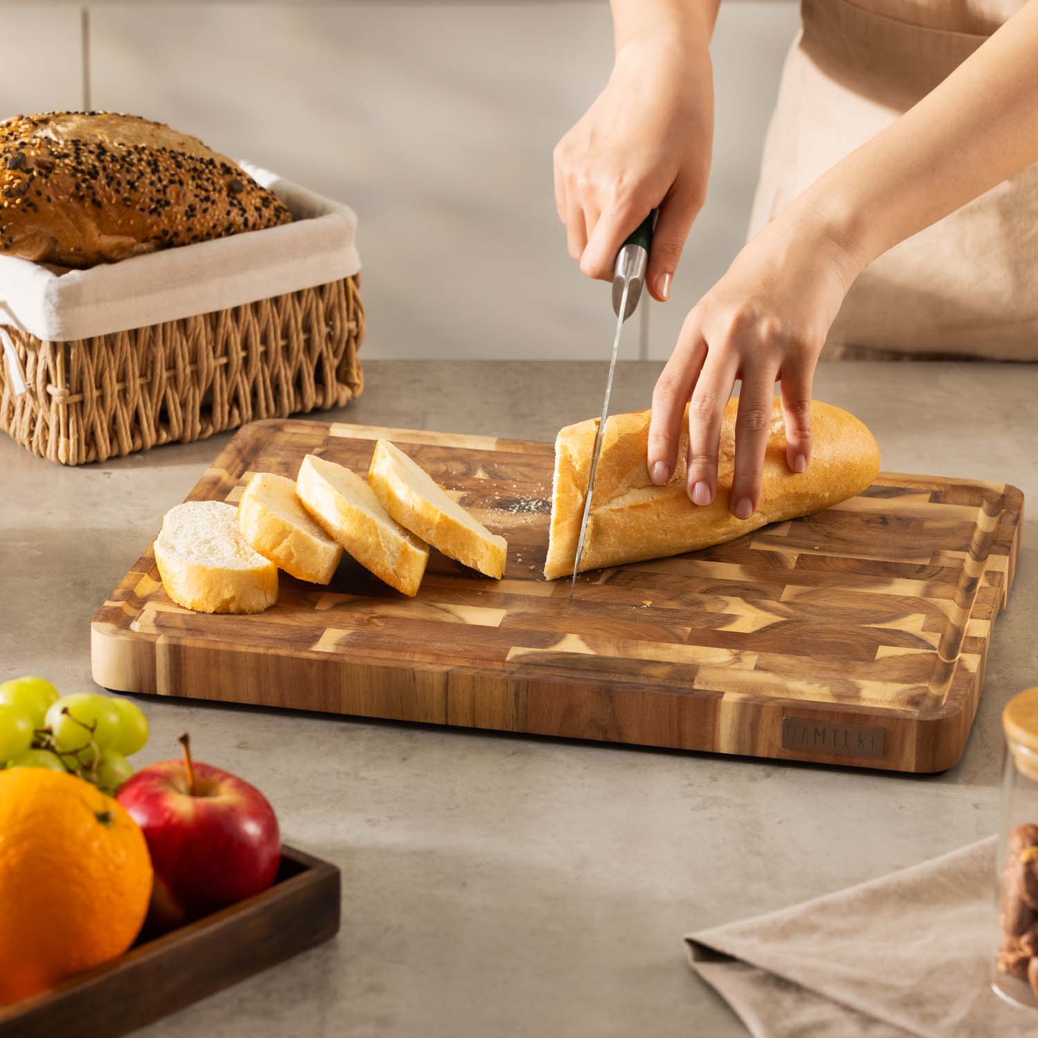 Persoon die een wit brood snijdt op een houten snijplank. Ook brood, fruit en een theedoek in beeld