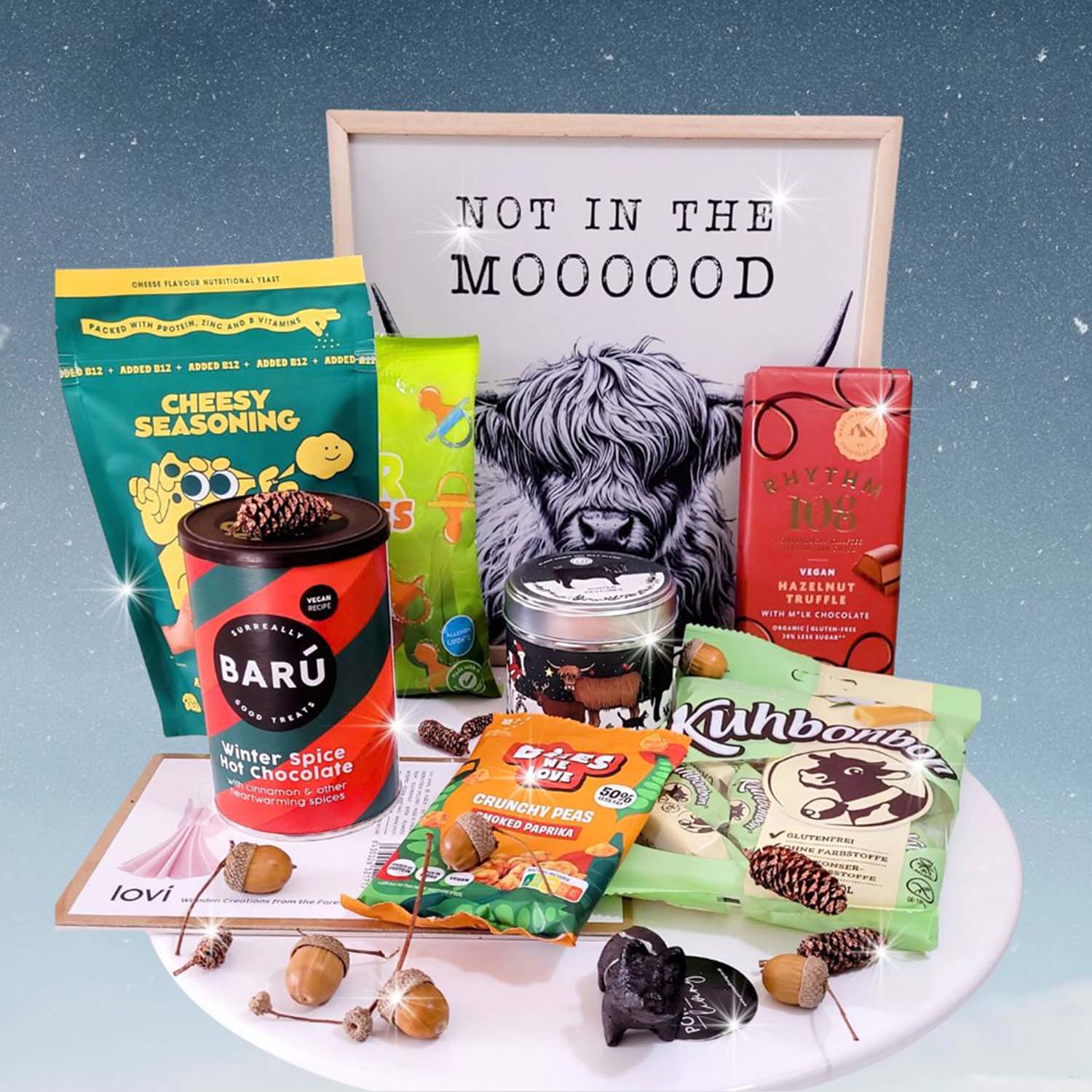 Kerstpakket van webshop tAK met allerlei producten, o.a. een winter spice hot chocolate of een reep vegan hazelnoot chocola. Met sterretjes op de achtergrond